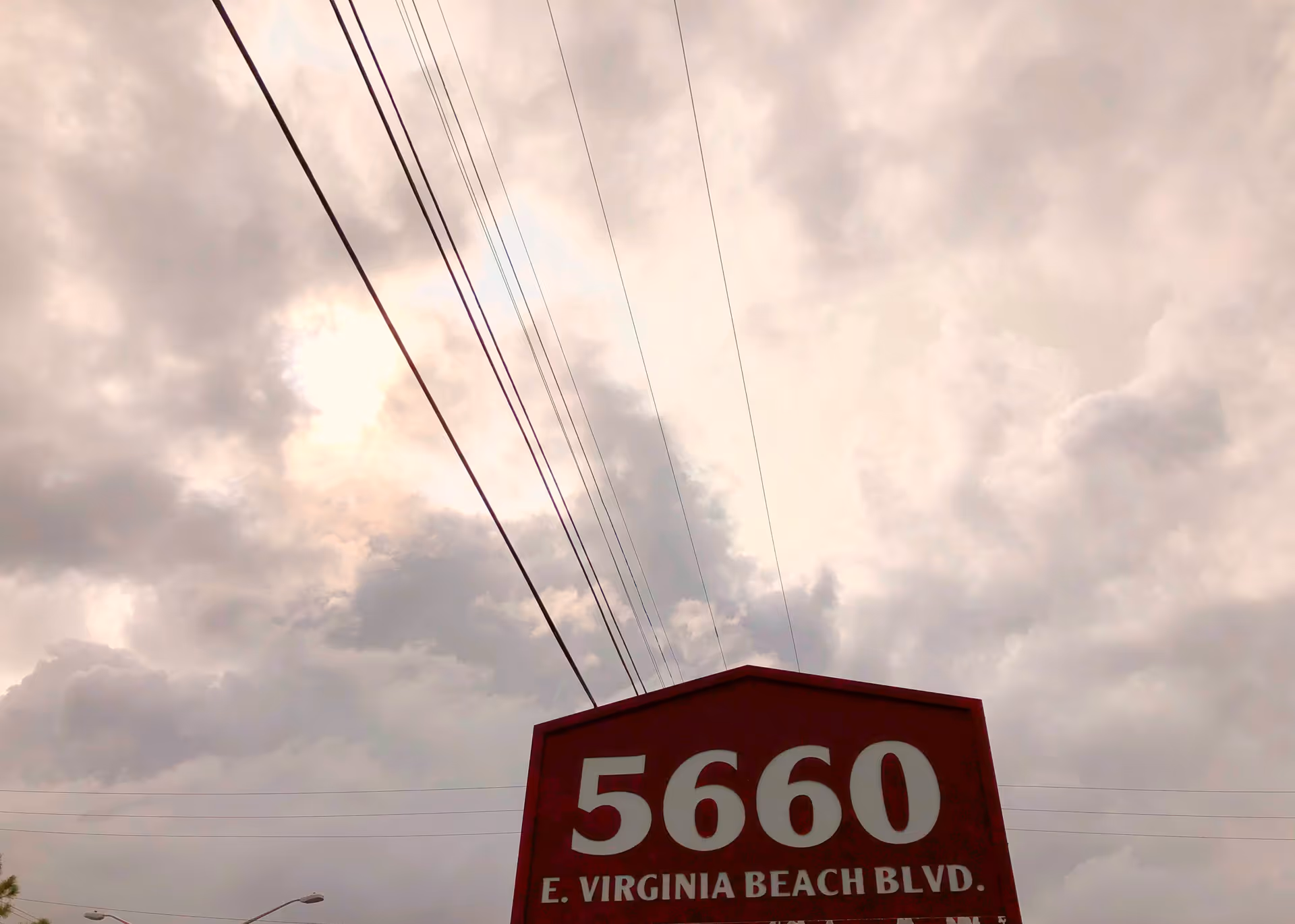 Red street sign reading 5660 E. Virginia Beach Blvd with power lines overhead.