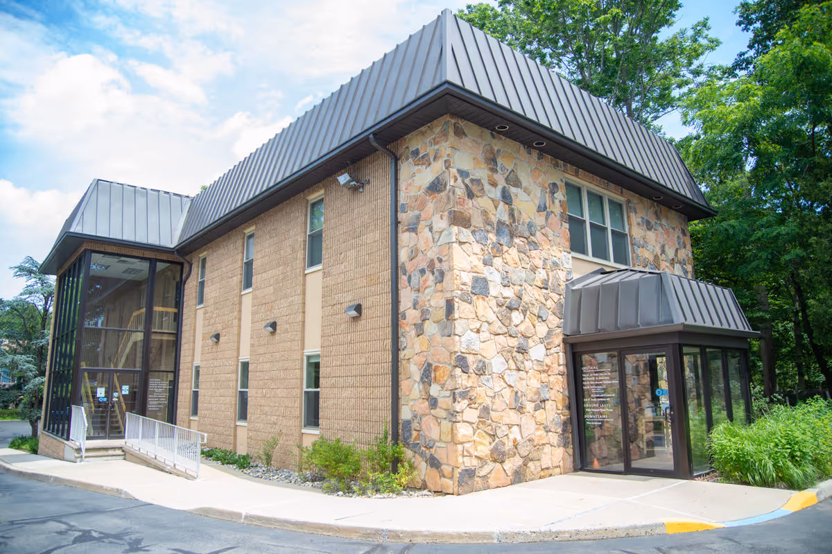 Two-story stone and brick senior living facility exterior with glass entrance and surrounding trees.