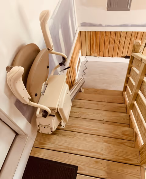 A beige stairlift attached to a wooden staircase in an indoor residential hallway.