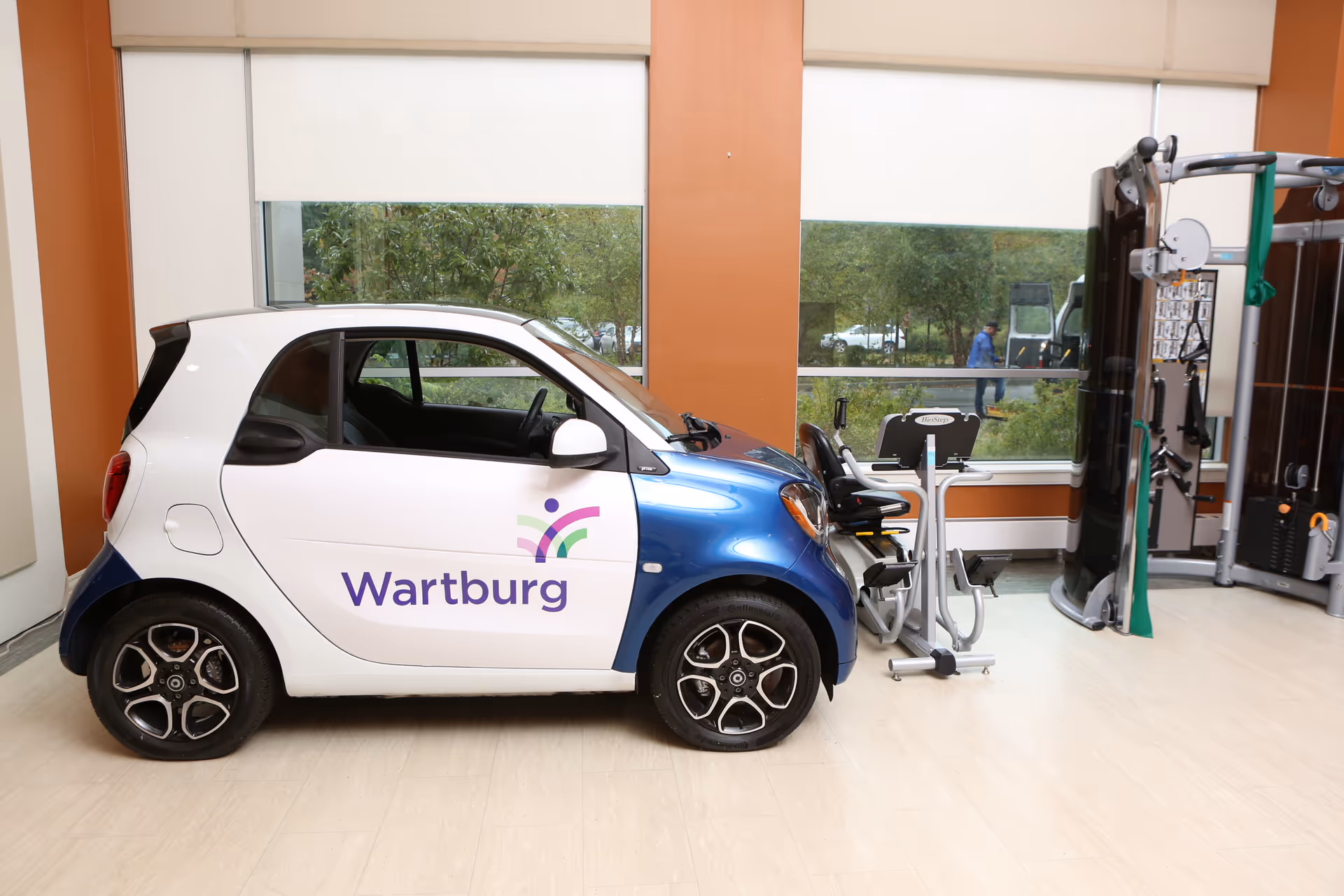 A Wartburg branded compact car sits indoors beside gym equipment.