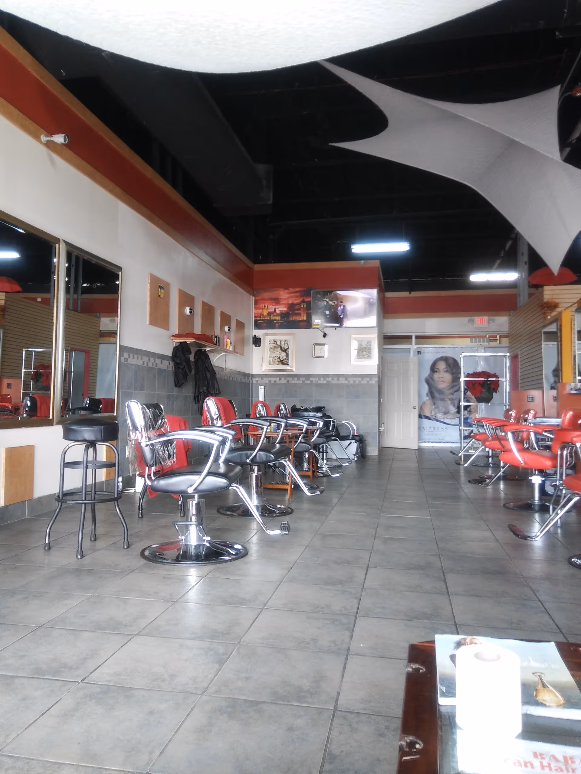 Hair salon interior with red and black barber chairs along tiled floor.