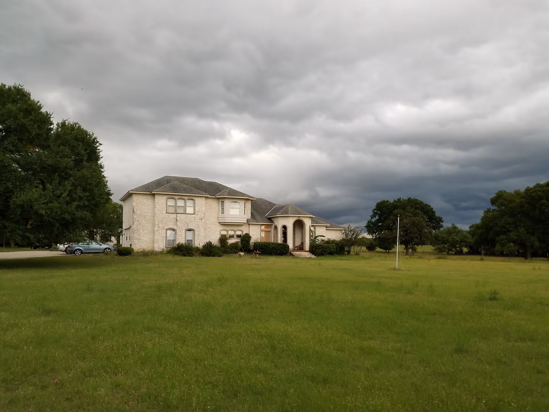 Stone two-story building with arched entry sits on a grassy field under cloudy skies.