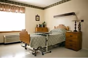 Hospital-style bedroom in a senior living facility with a bed, dresser, and window.