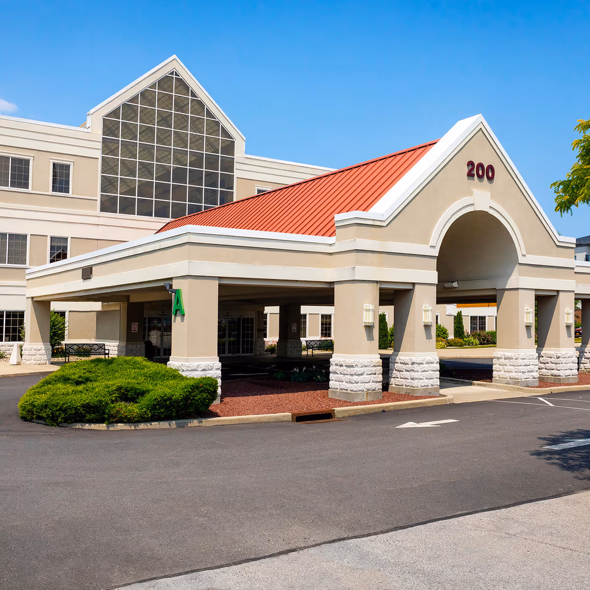 Front view of a beige medical facility with a red roof and glass entrance.