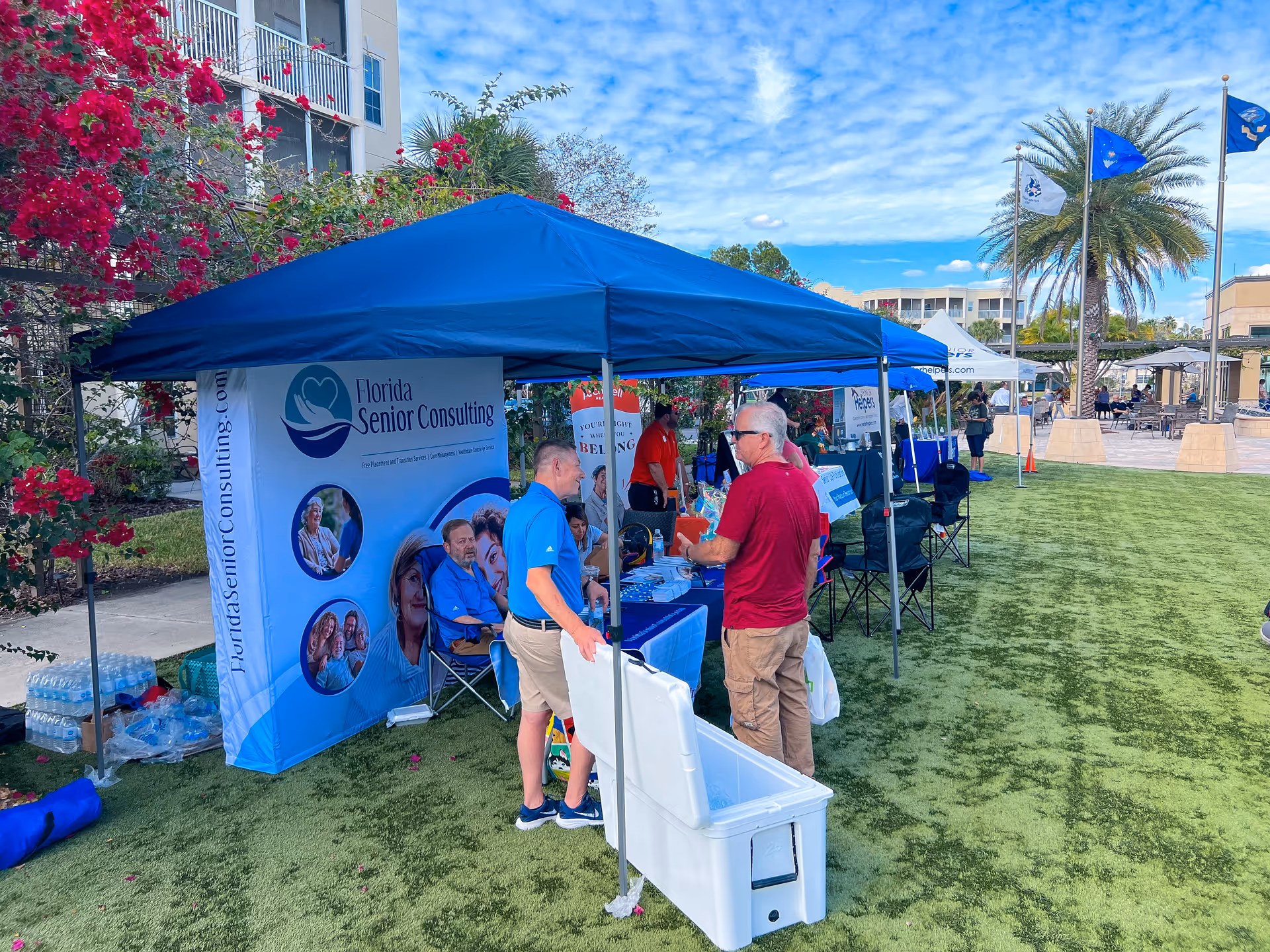 Outdoor booth setup with Florida Senior Consulting banners and people under blue canopies.