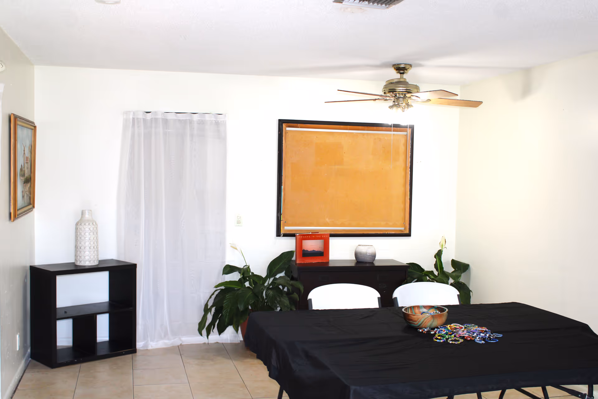 A dining room setup with a black tablecloth, white chairs, plants, and wall decor.
