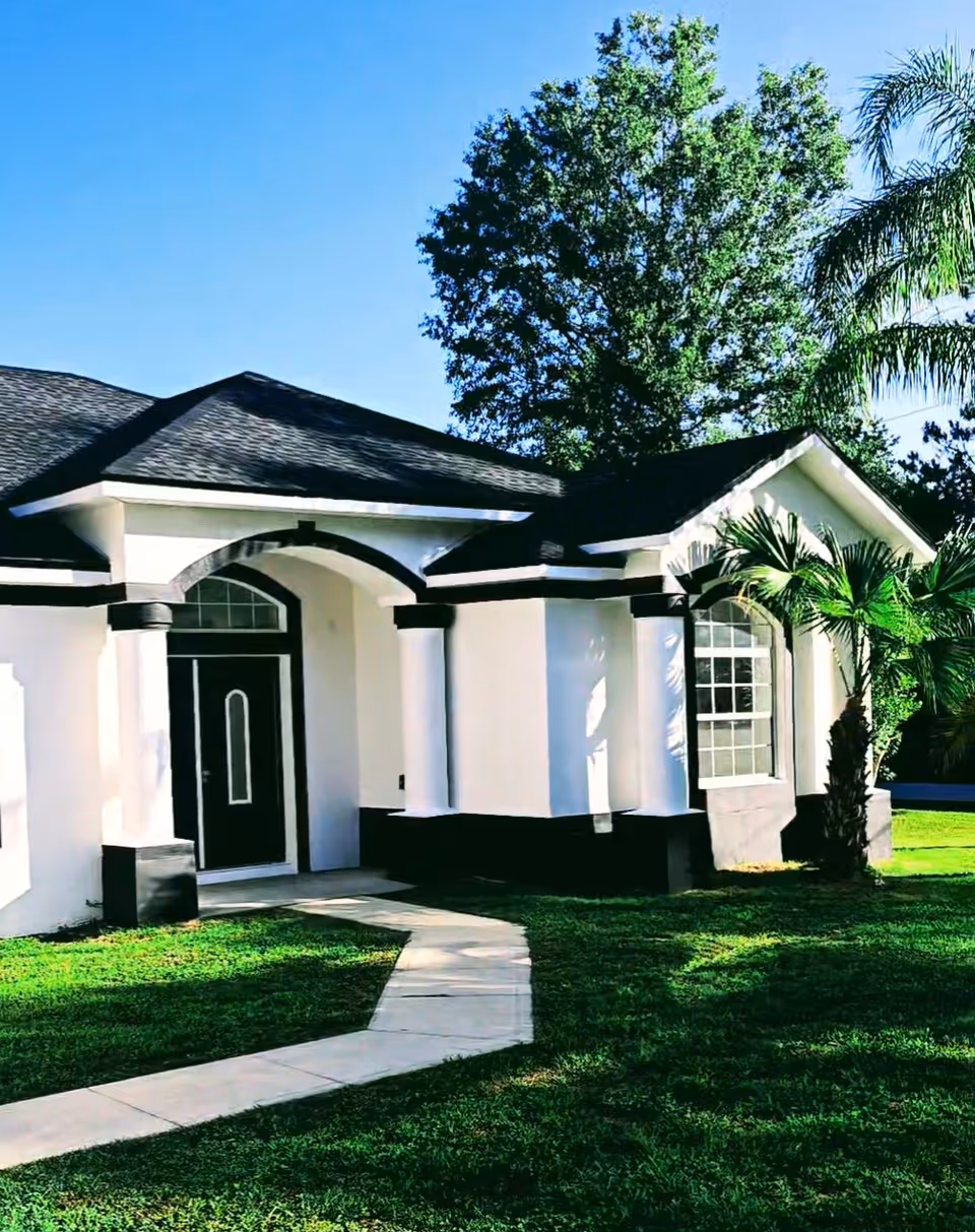 White building front with columns, curved walkway, and palm trees on lawn.