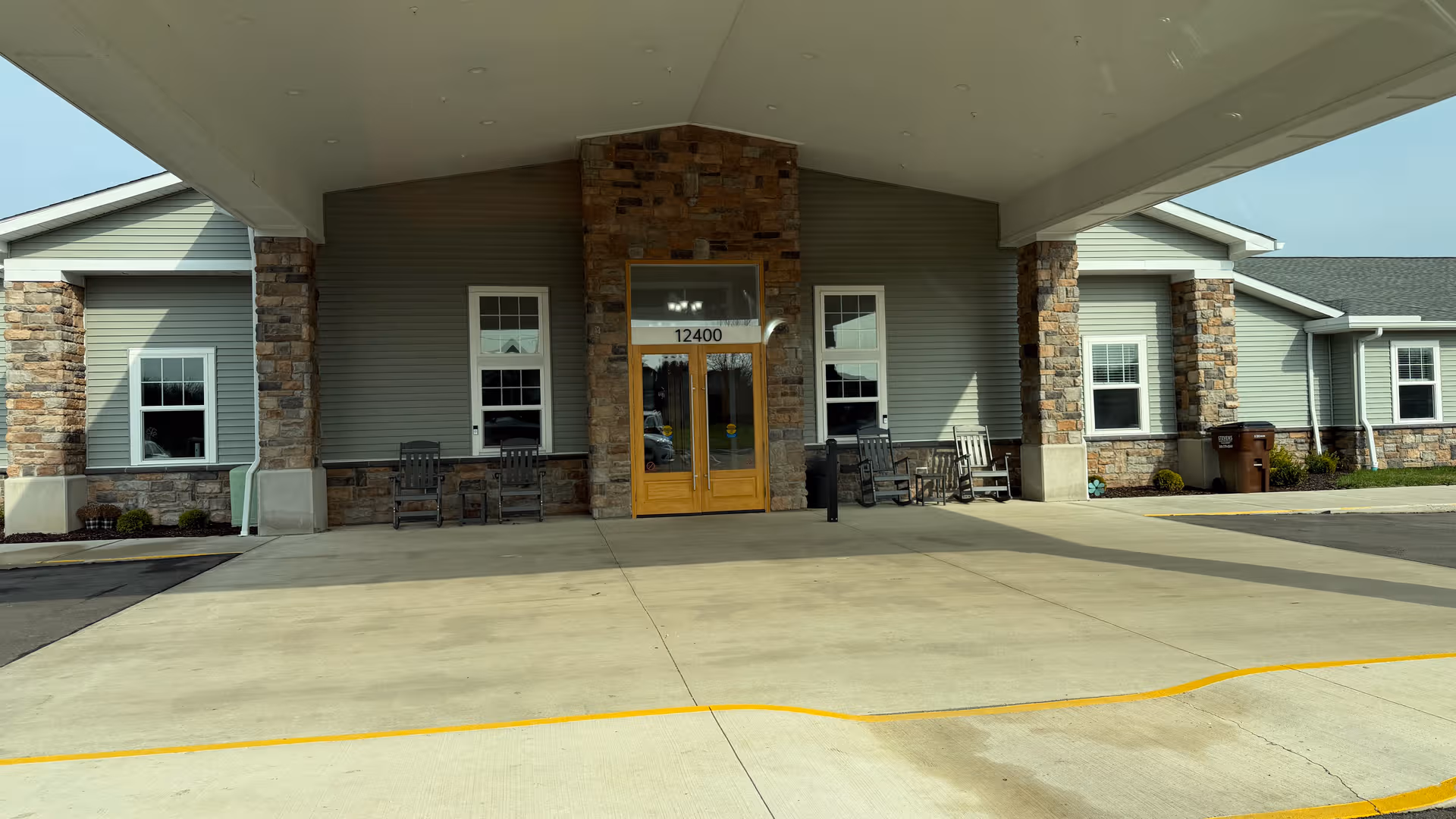 Exterior view of a senior living facility entrance with stone pillars and seating.