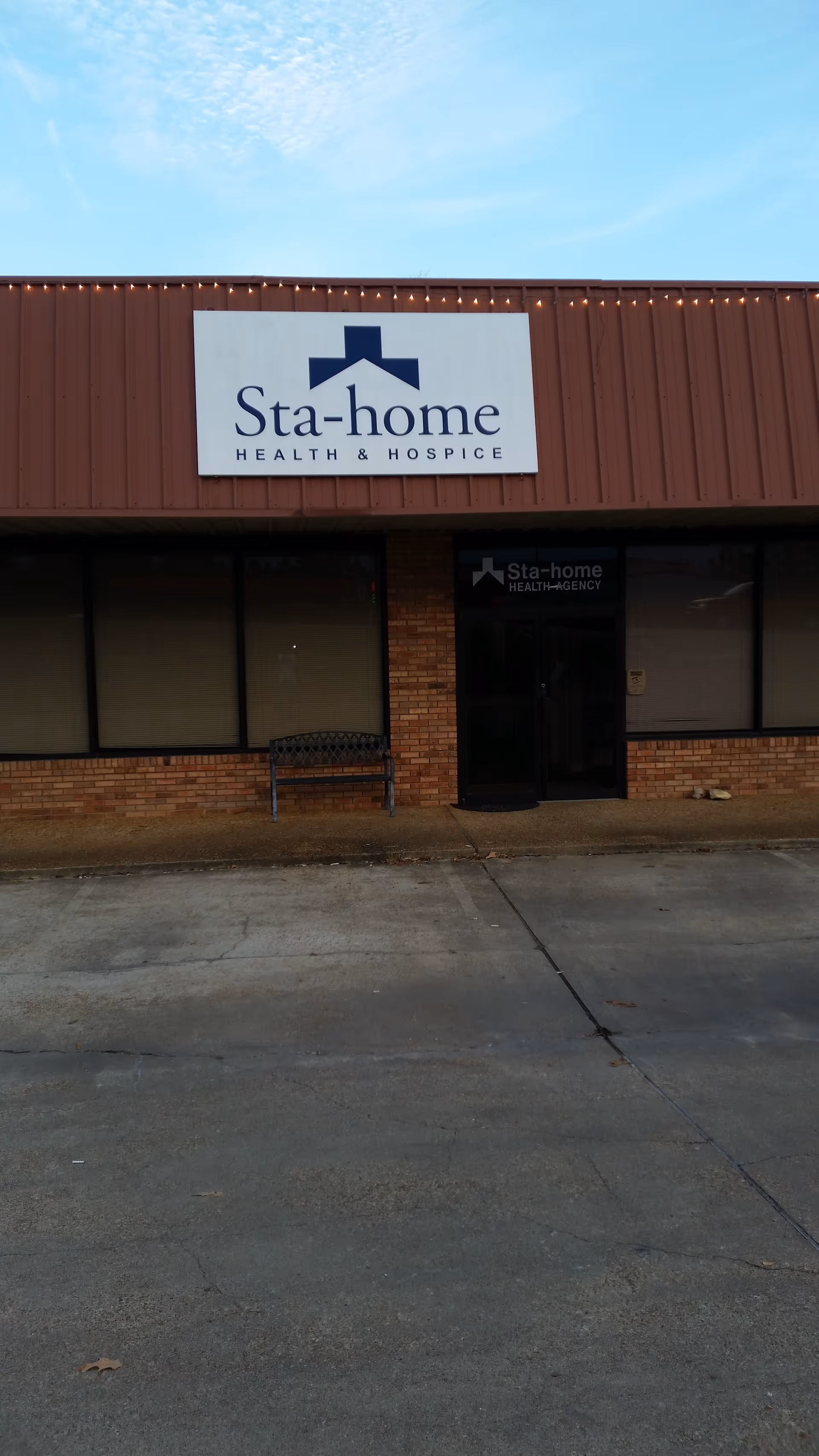 Exterior front of Sta-Home Health Agency building with sign and bench.
