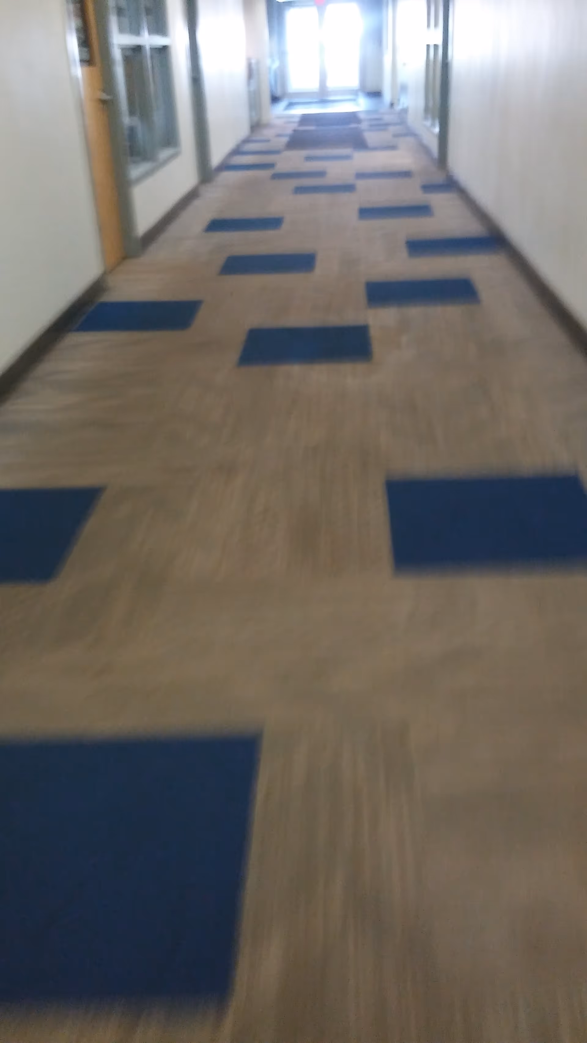 Long interior hallway in a senior living facility with blue floor mats.