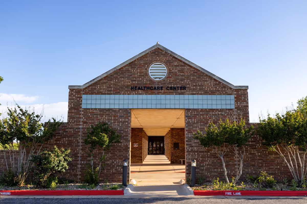 Front view of a brick healthcare center with central entrance and surrounding trees.