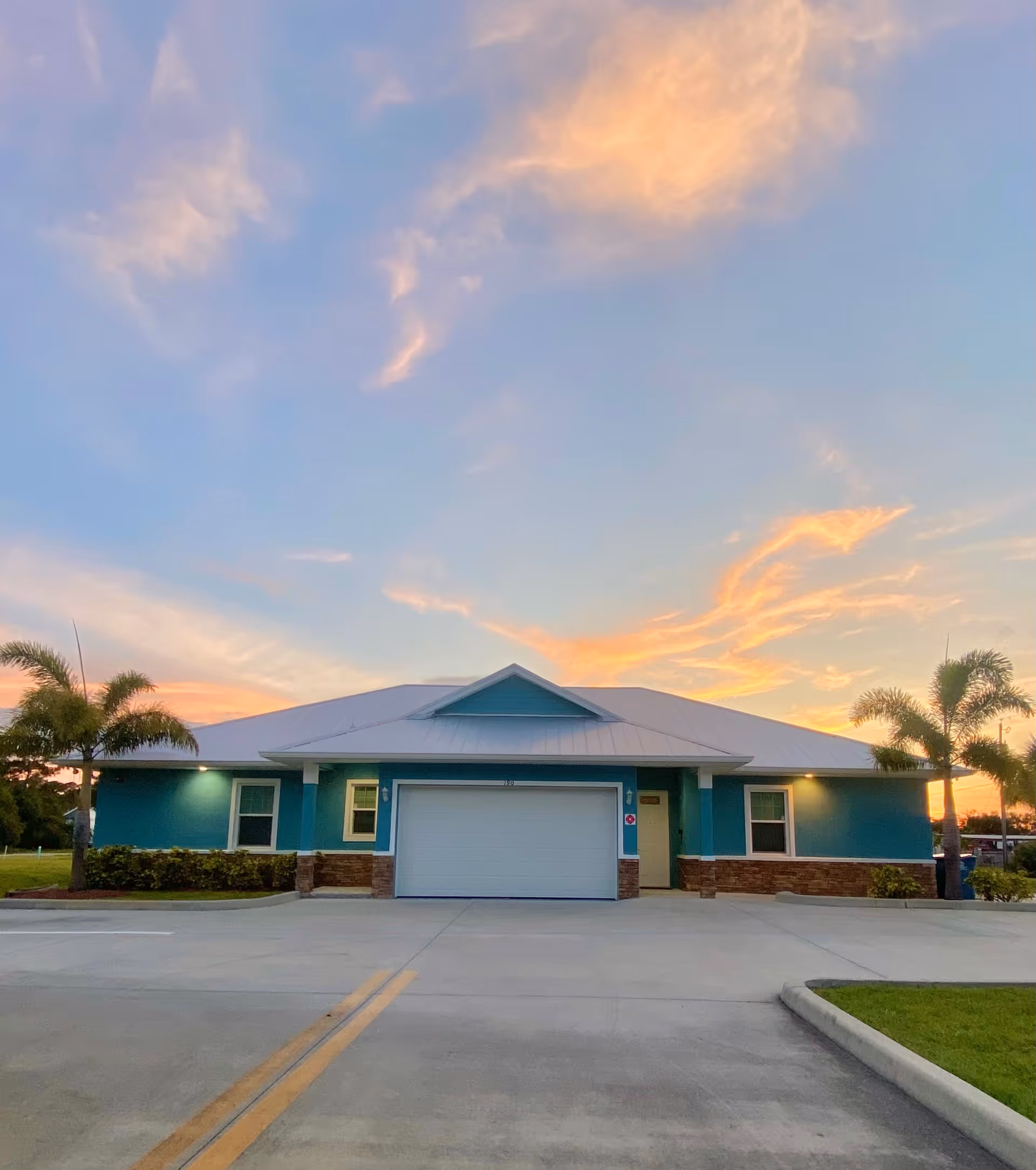 Front exterior of a teal assisted living facility at sunset with palm trees.