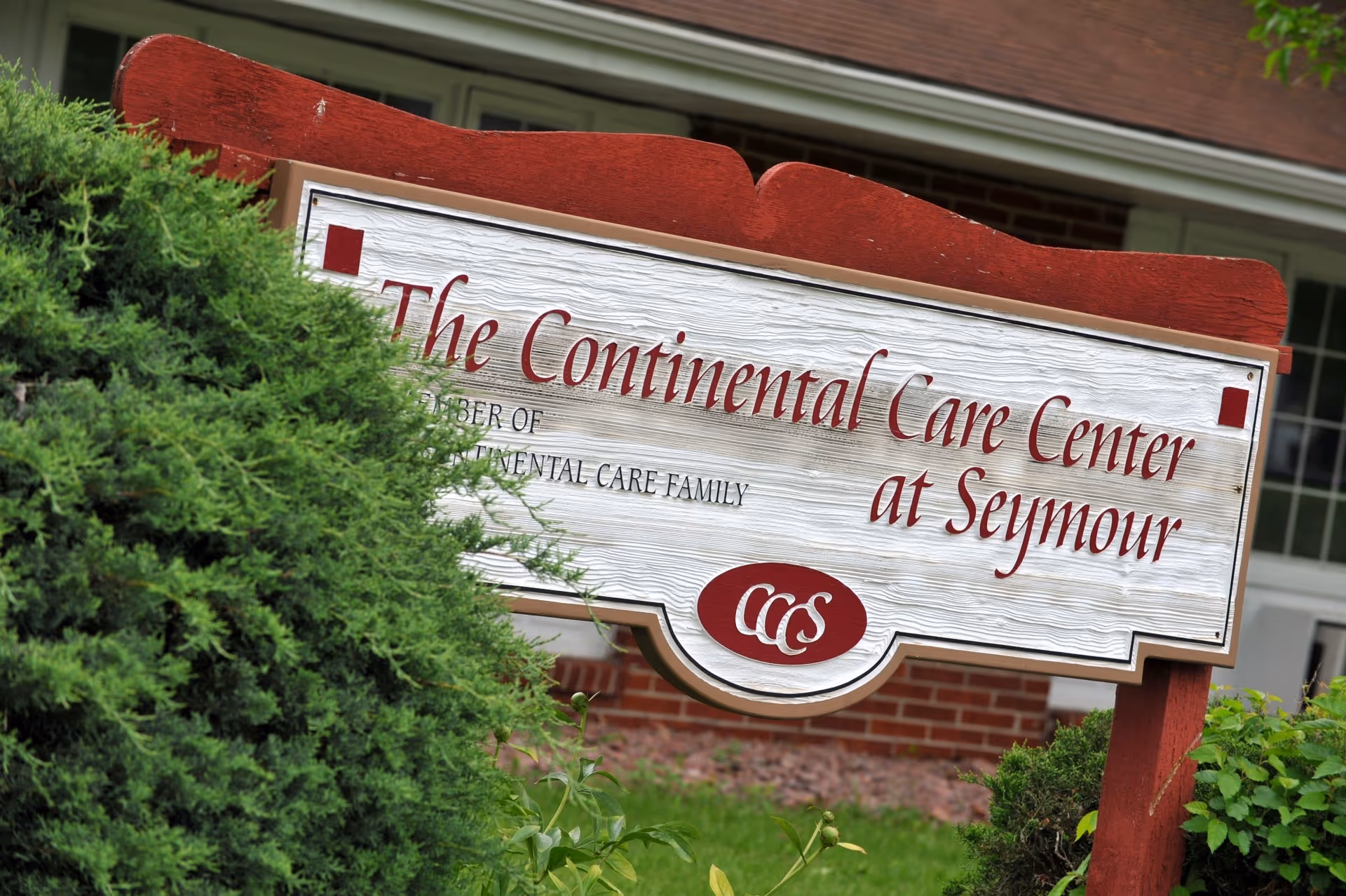 A large wooden sign reading The Continental Care Center at Seymour, framed by bushes.