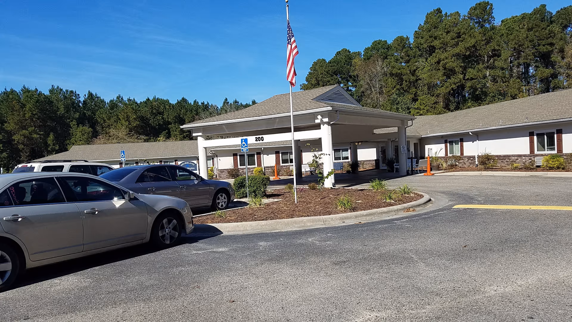 Exterior view of Shoreland Health Care & Retirement building with parking, front entrance, and flagpole.