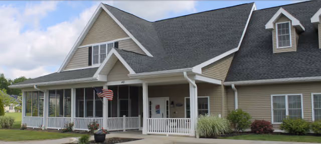 Beige Heritage Plaza Apartments building with front porch, white railings, and American flag.