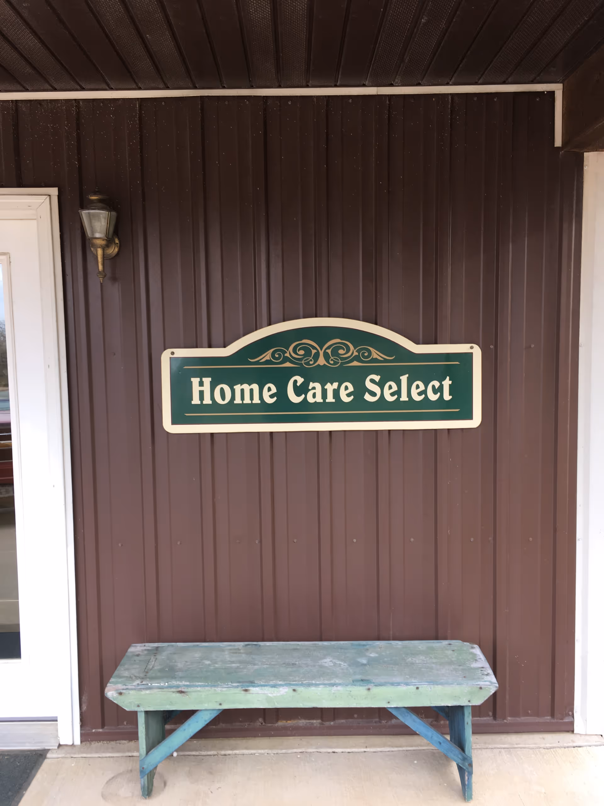 Exterior view of Home Care Select entrance with green sign and weathered bench