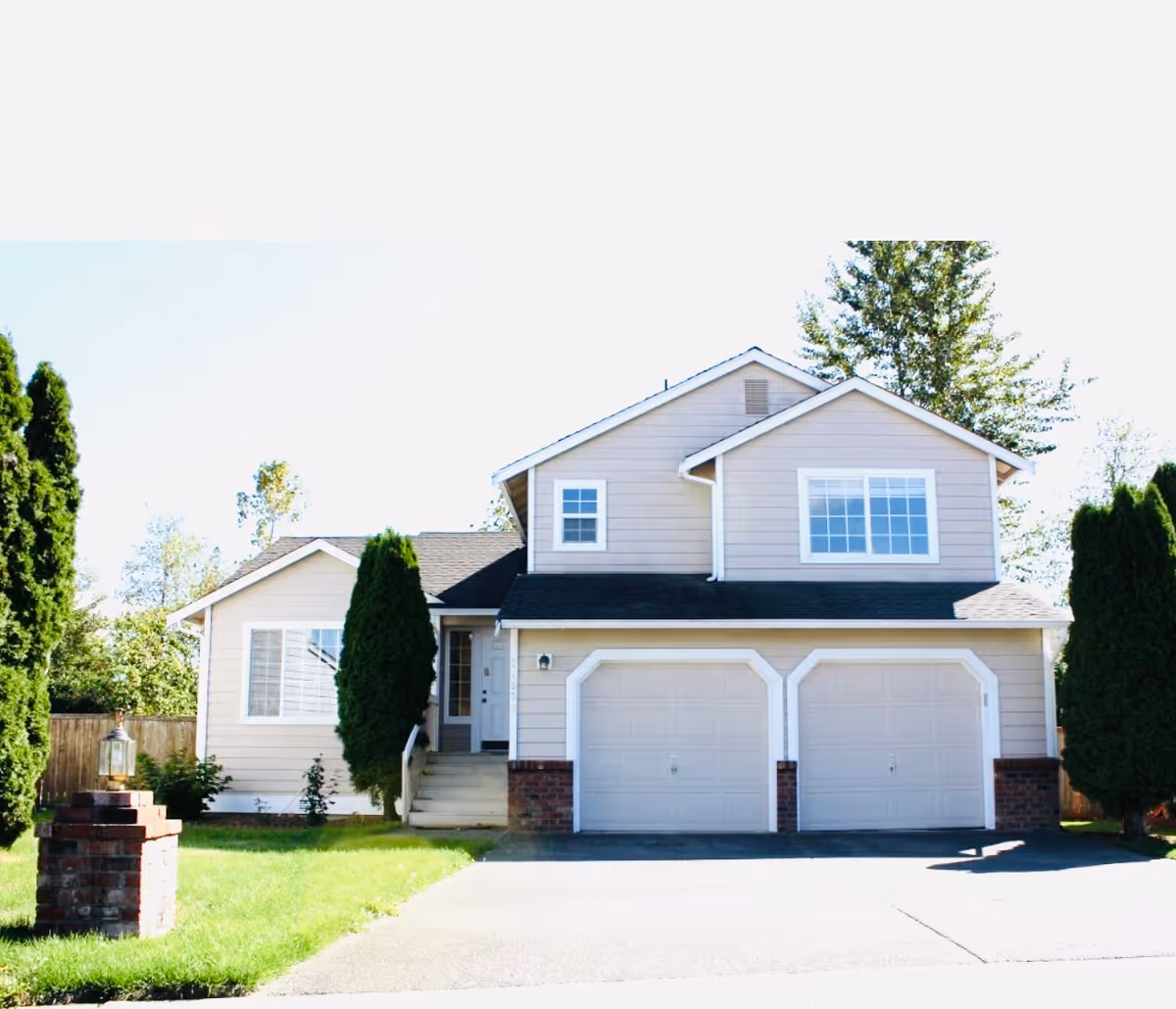 Front view of a two-story beige house with twin garage doors and a green lawn.
