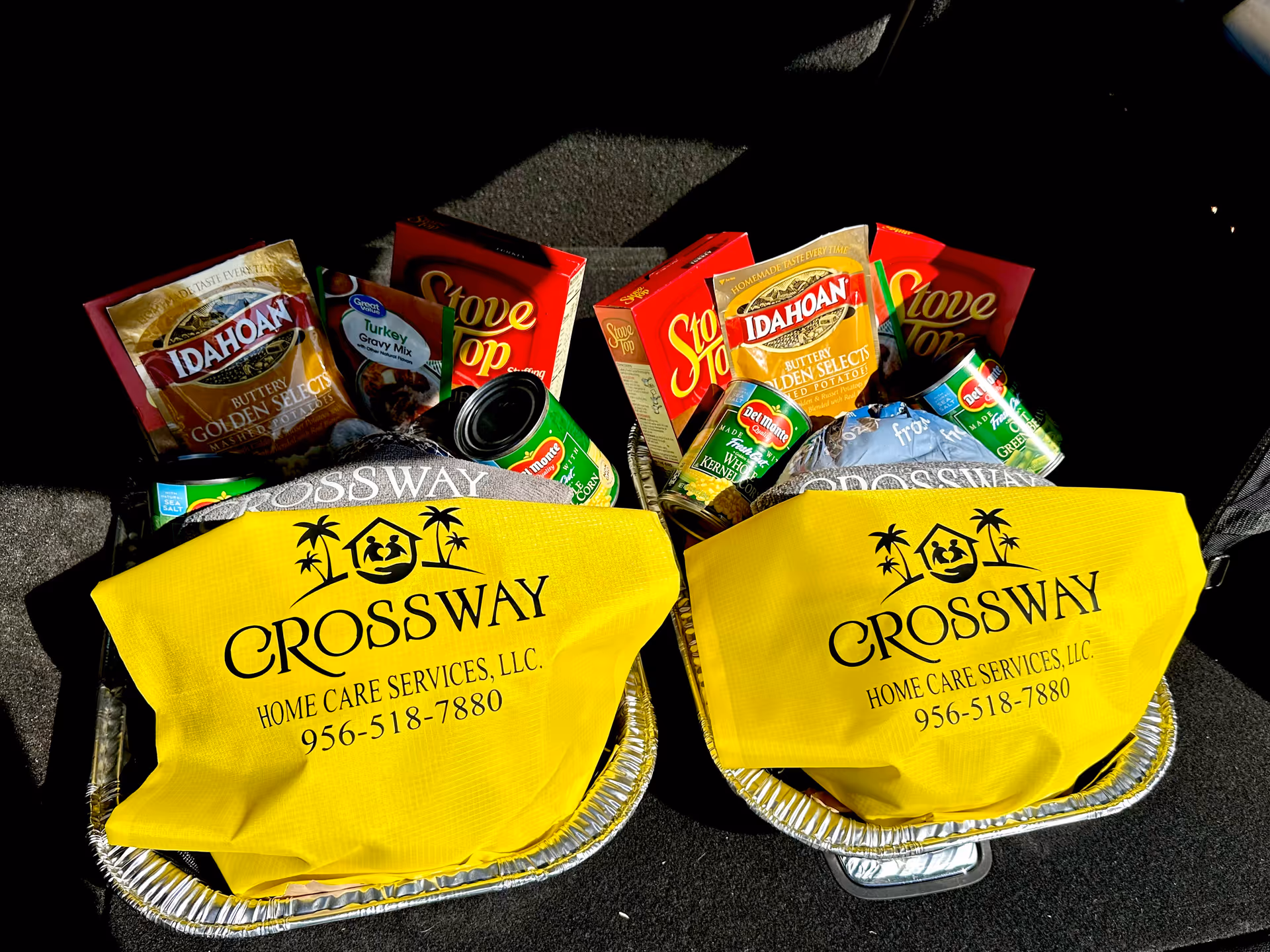 Two yellow Crossway Home Care bags filled with boxed groceries sit in a car trunk.