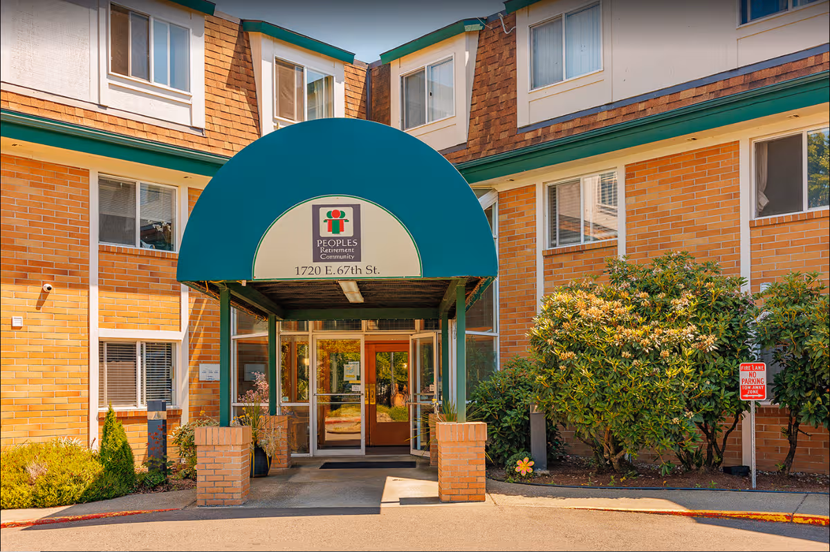 Brick senior living facility entrance with teal curved canopy and glass doors.