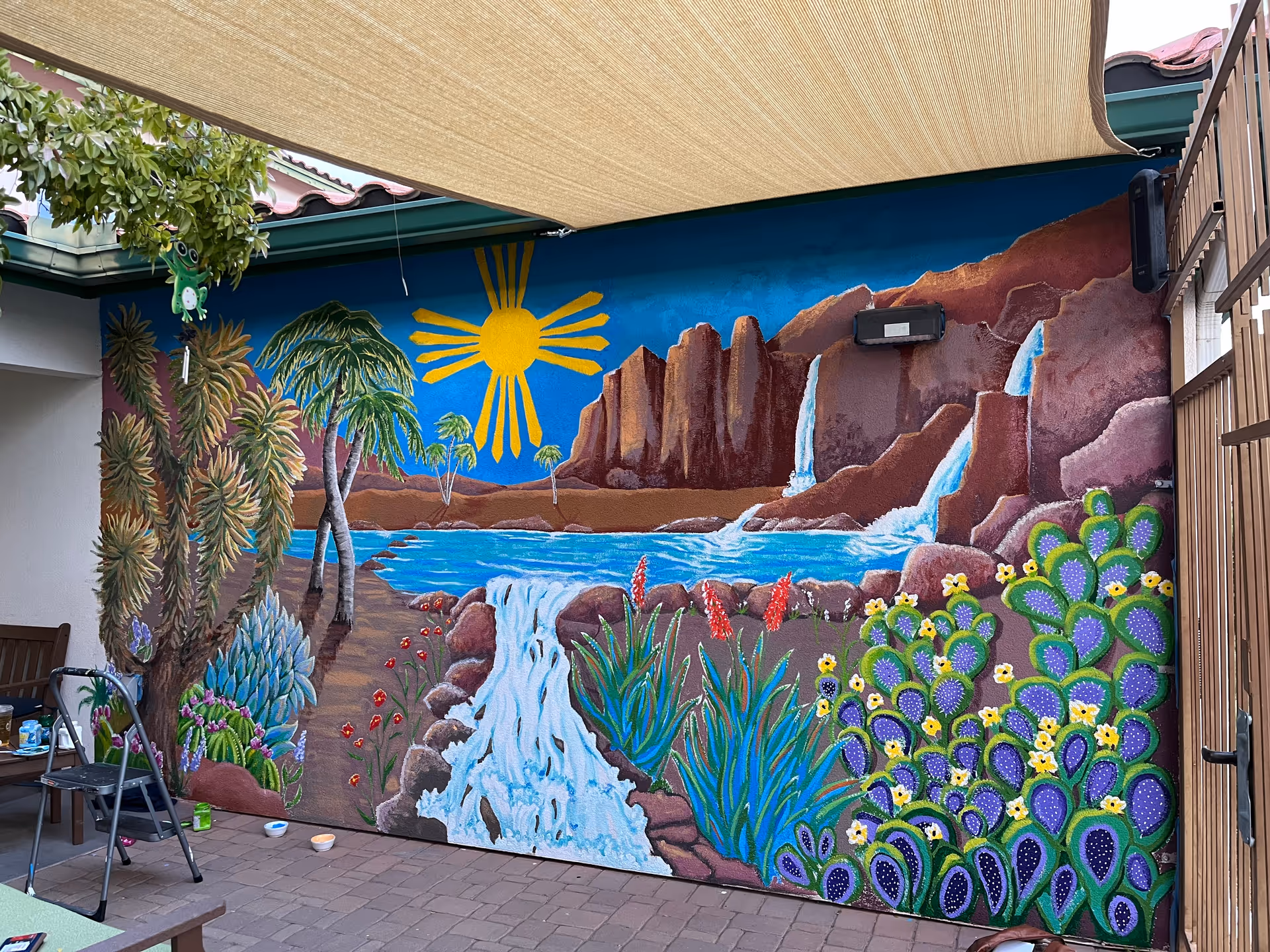 Outdoor courtyard mural depicting a desert scene with cacti and a waterfall.