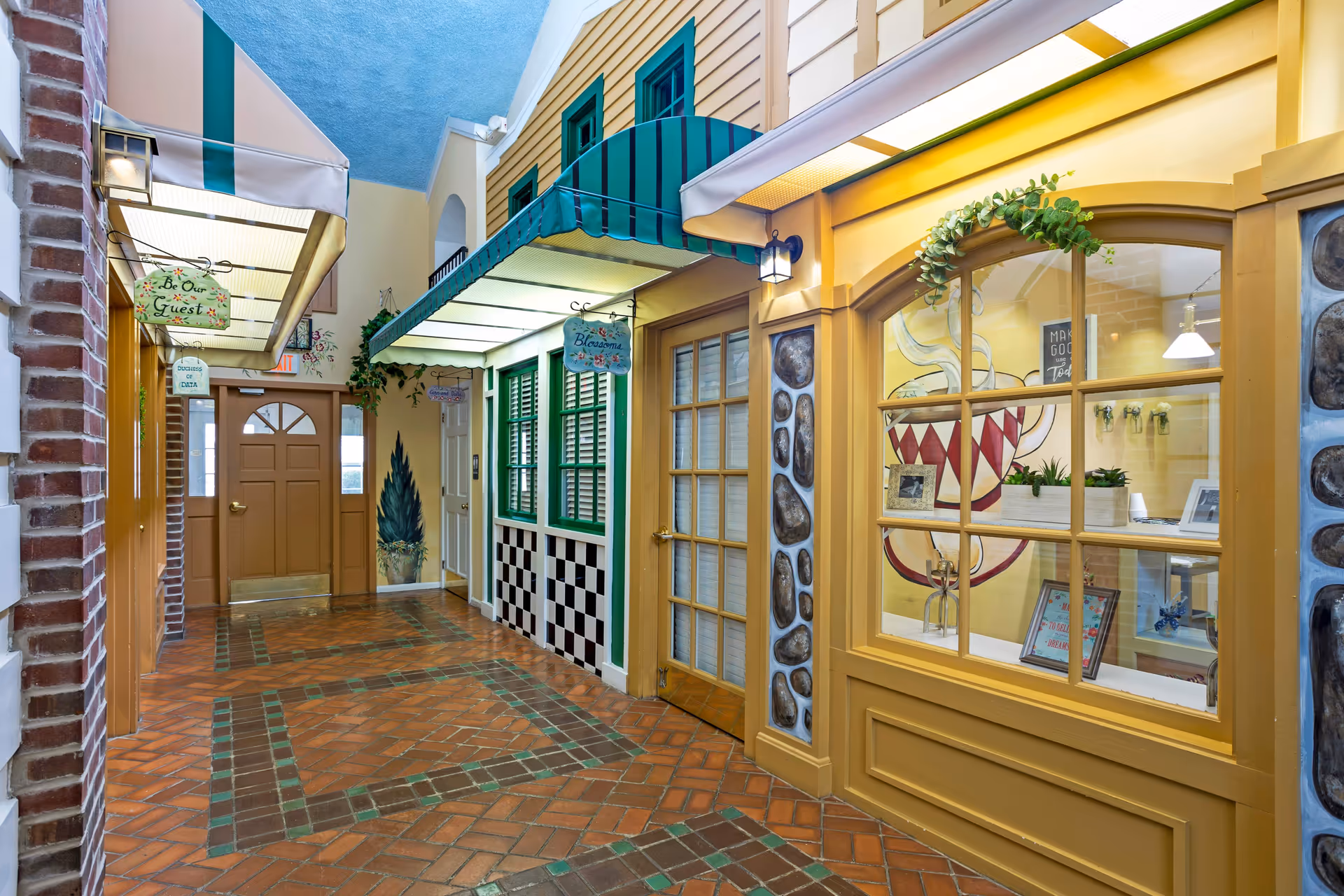 Indoor corridor designed like a small storefront street with awnings, display windows, and a decorative tiled floor.