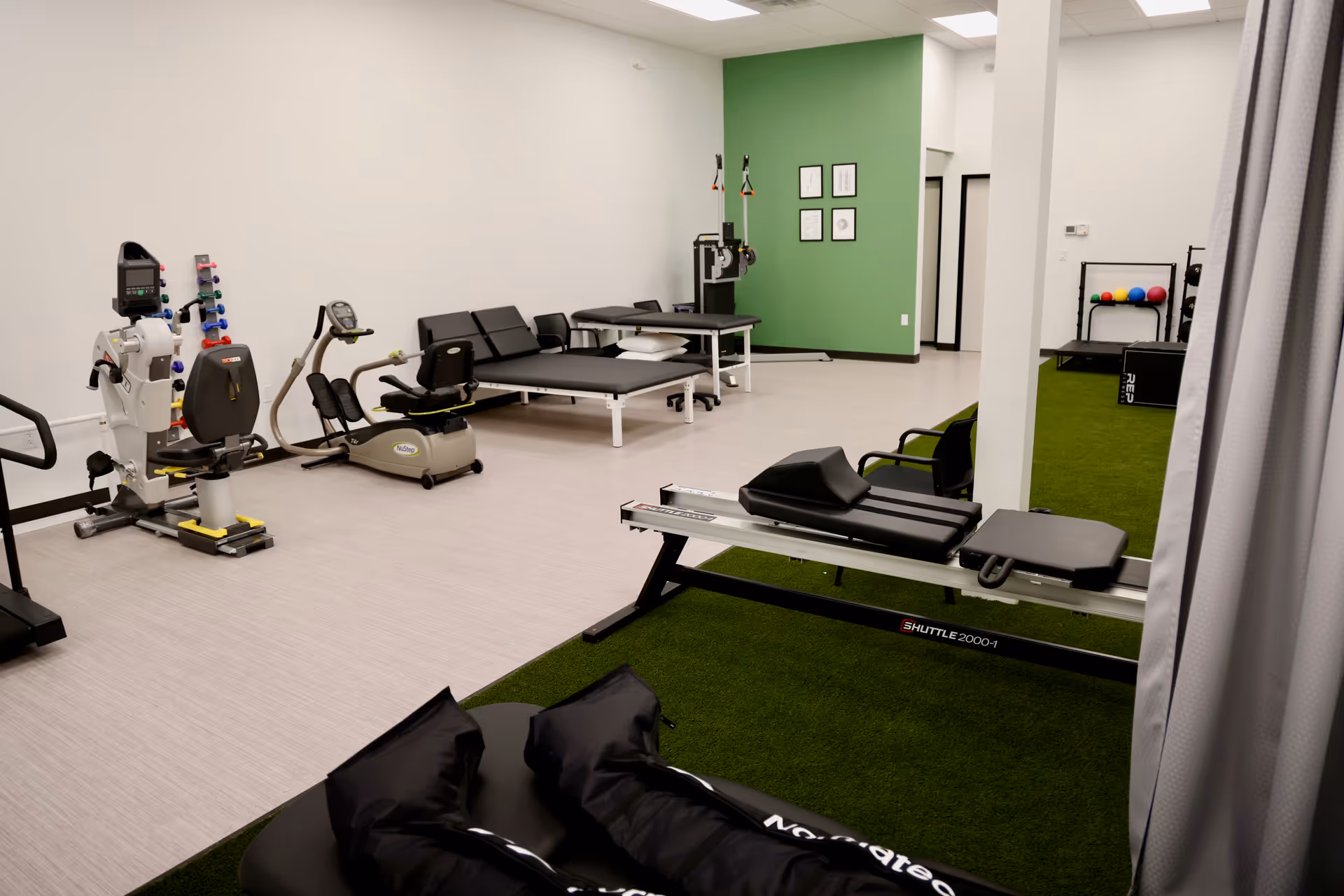 Interior rehab and wellness gym with exercise machines and therapy areas against a green wall.
