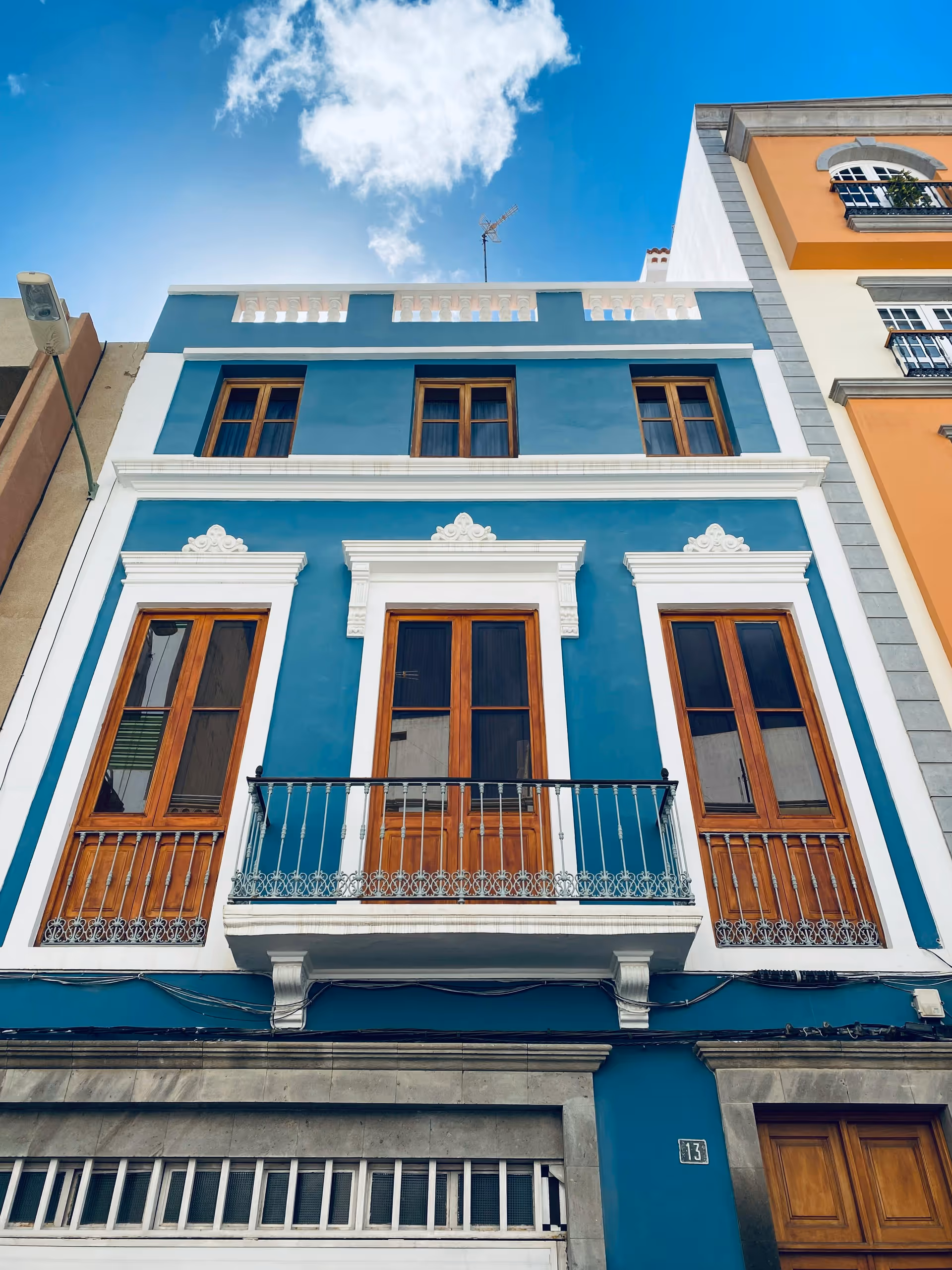 Blue building facade with white trim, wooden doors, and a small balcony.