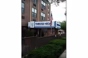 Brick nursing center with front entrance sign, American flag, and surrounding hedges.