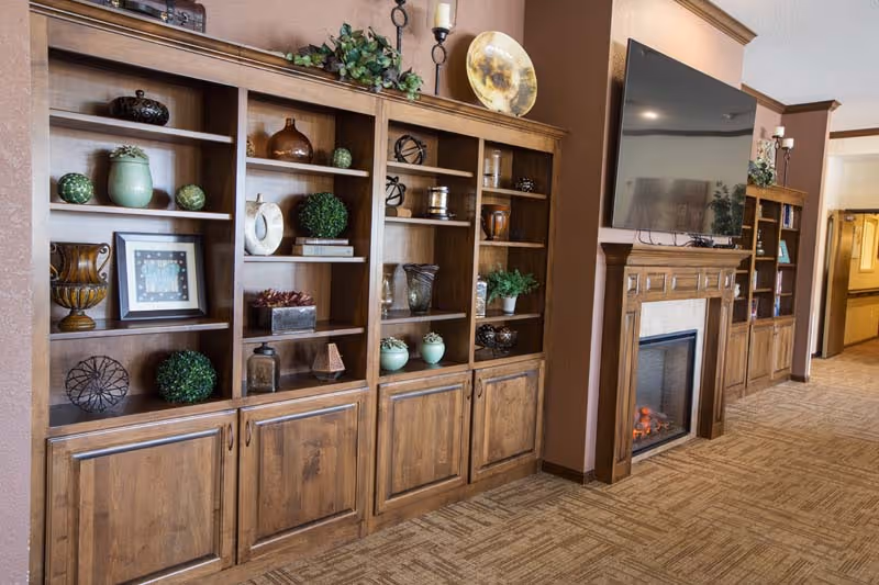 Wooden built-in shelves with decorative items line a warm living room beside a fireplace and TV.