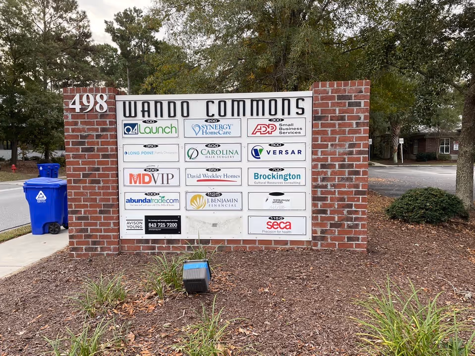 Exterior brick signboard for Wando Commons with multiple business logos and landscaping.