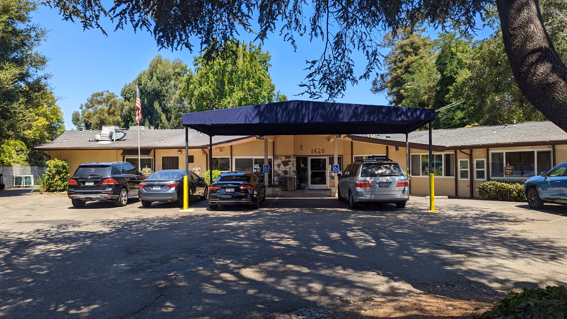 Front entrance of Windsor Gardens Care Center Hayward under a blue canopy with parked cars.