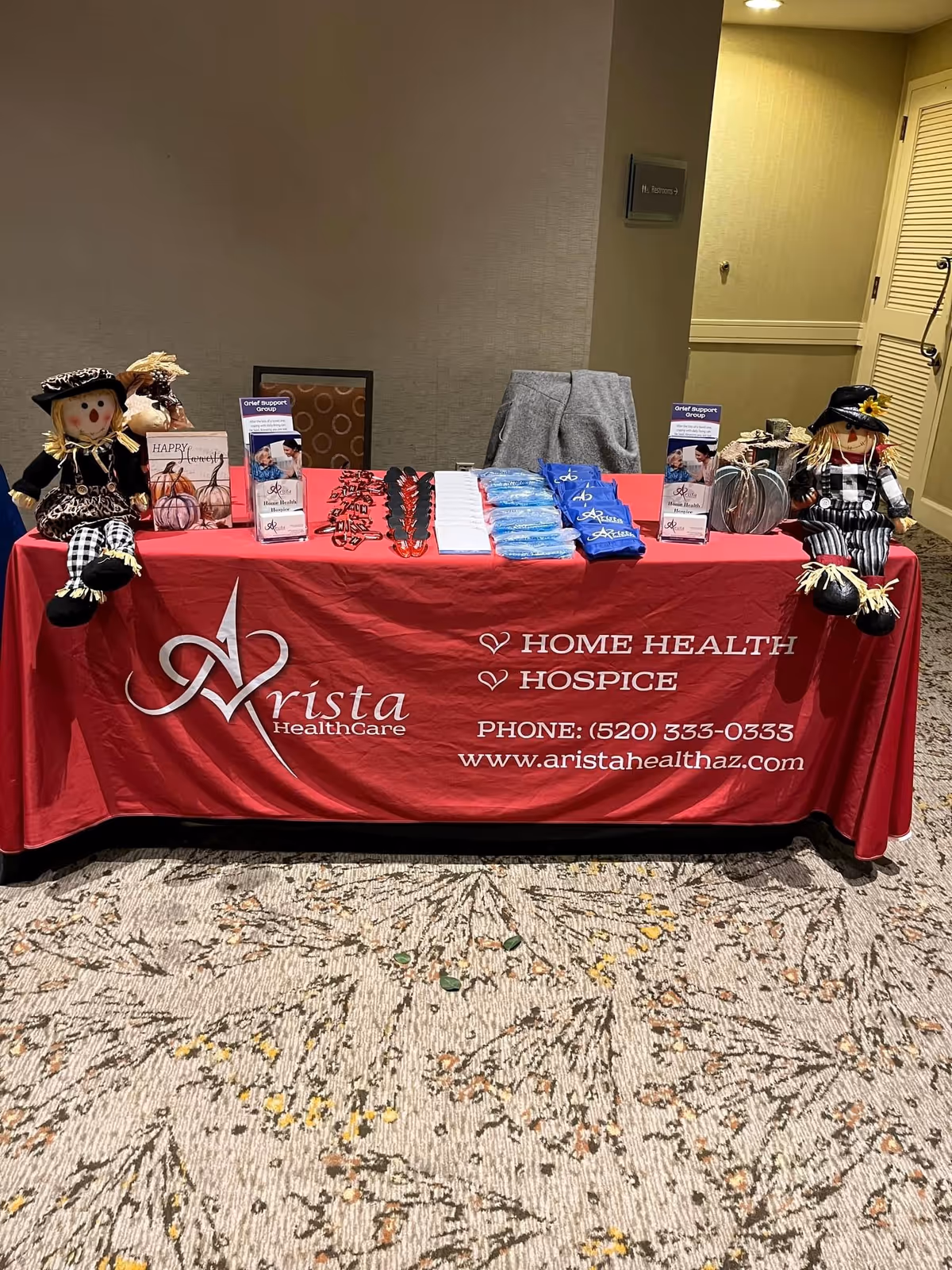 Arista Hospice & Healthcare table with brochures and fall scarecrows in a hallway.