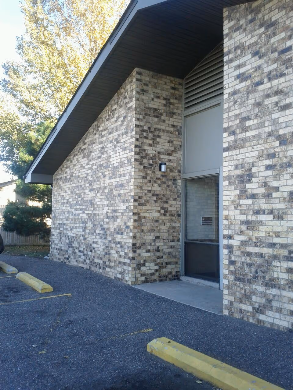 Brick exterior of a facility with a doorway and parking lot near trees
