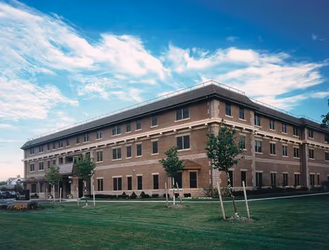 Brick senior living building exterior with lawn, trees, and blue sky.