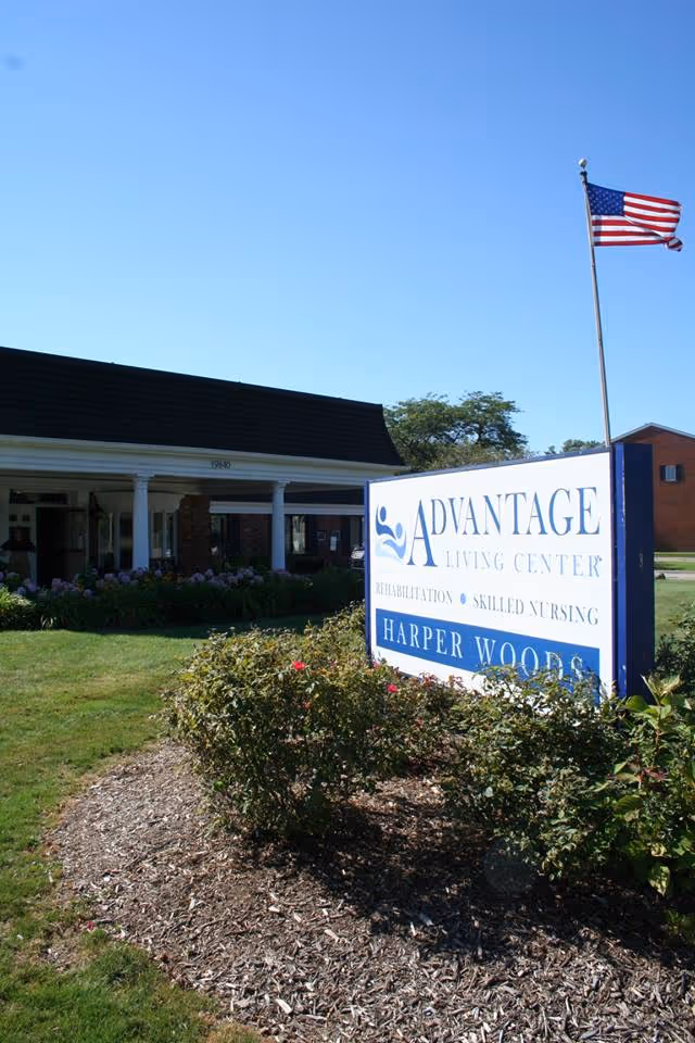 Front exterior of Advantage Living Center - Harper Woods with sign, flag, and landscaping.