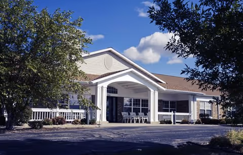 Front view of a single-story senior living facility with a covered entrance and chairs.