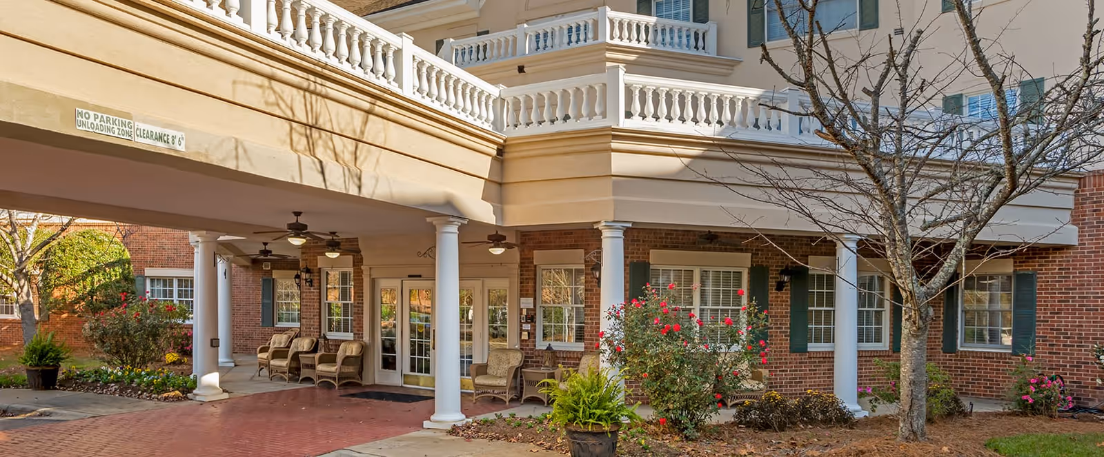 Brookdale South Charlotte exterior: brick building with white columns, porch seating, and manicured shrubs.