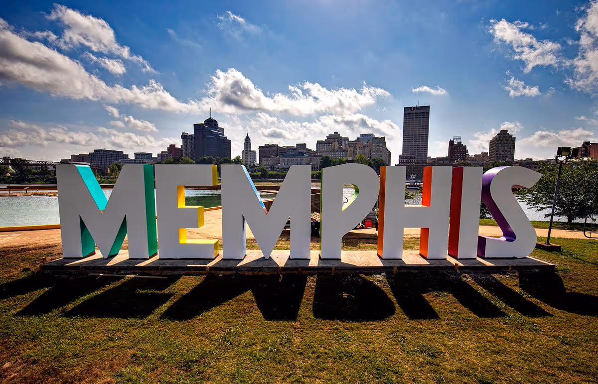 Large colorful MEMPHIS letters on a grassy park with city skyline in background