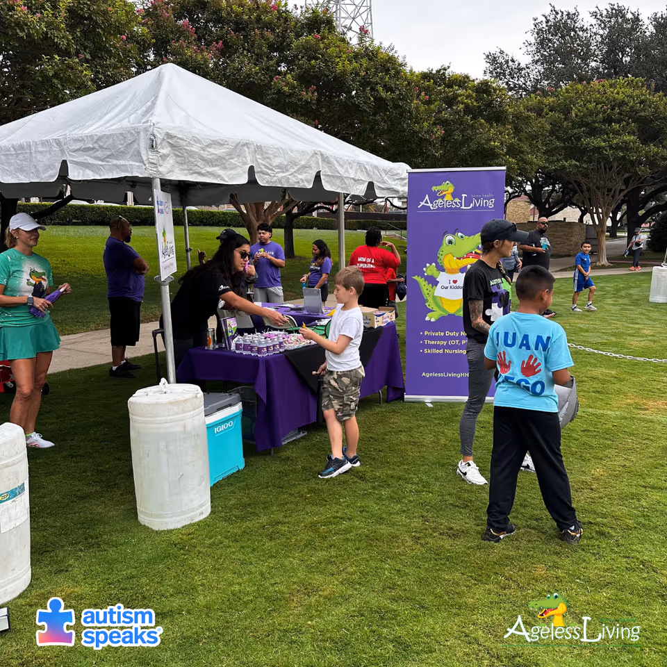 Outdoor event with a white tent, purple Ageless Living banner, and attendees.