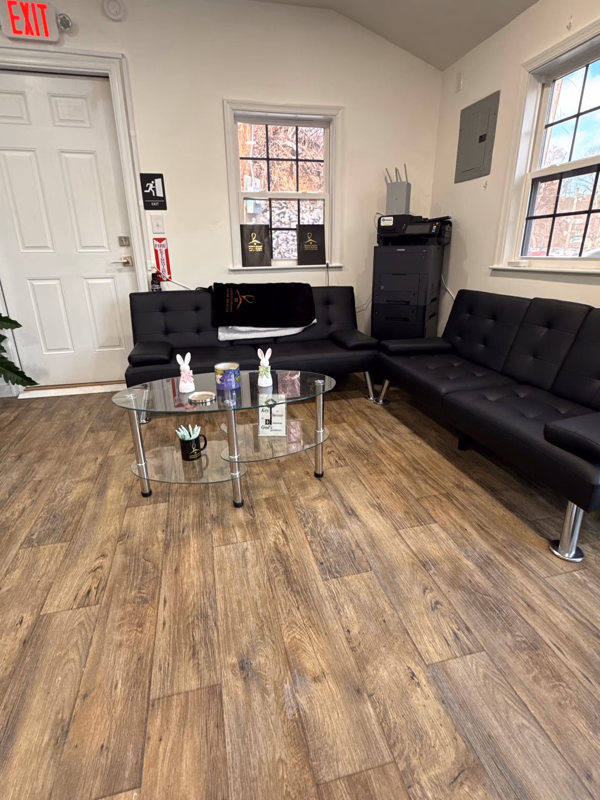 A modern indoor waiting lounge with black leather sofas and a glass coffee table.