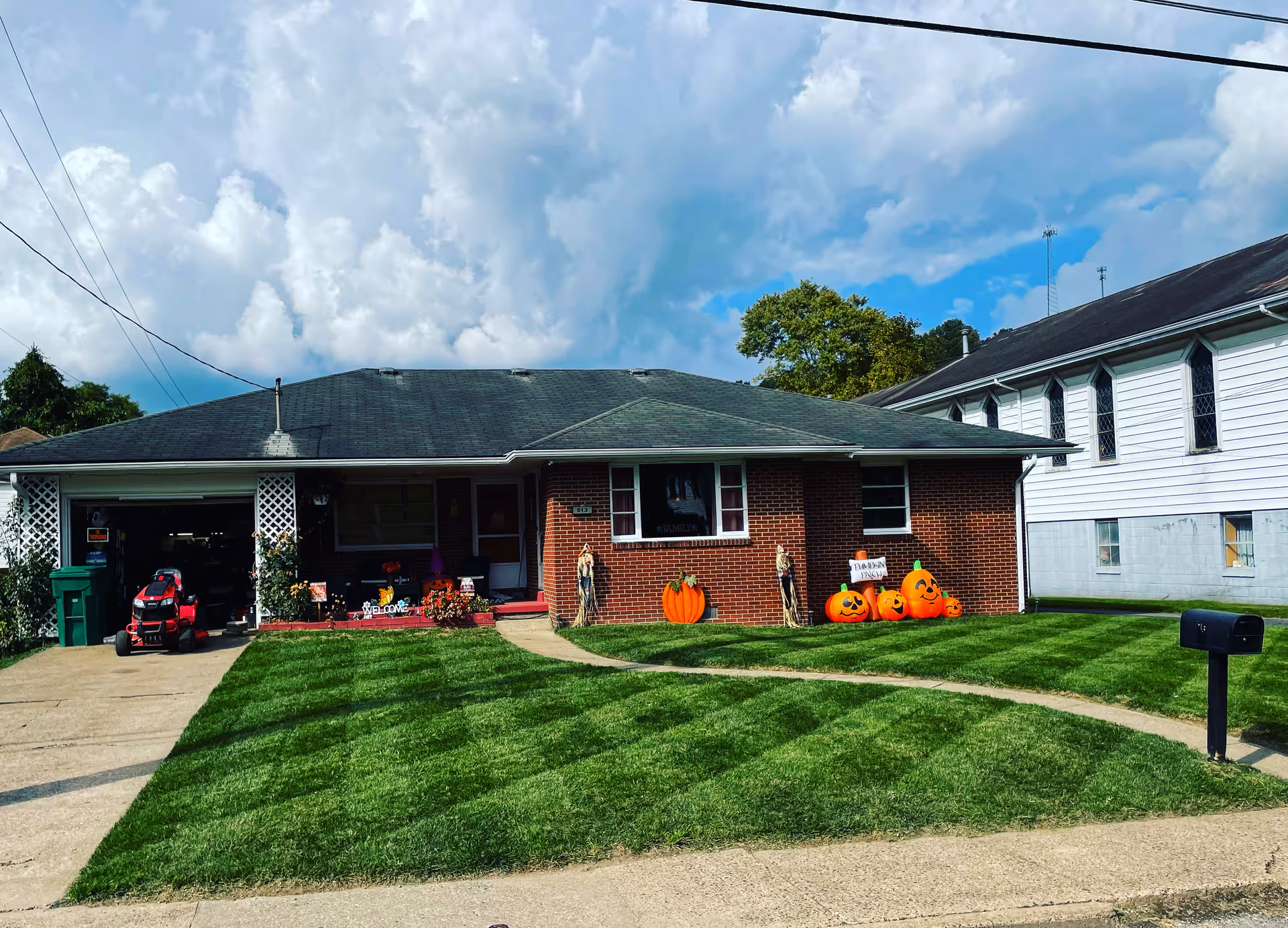 A single-story brick house with a well-manicured lawn and Halloween pumpkins near the entrance.