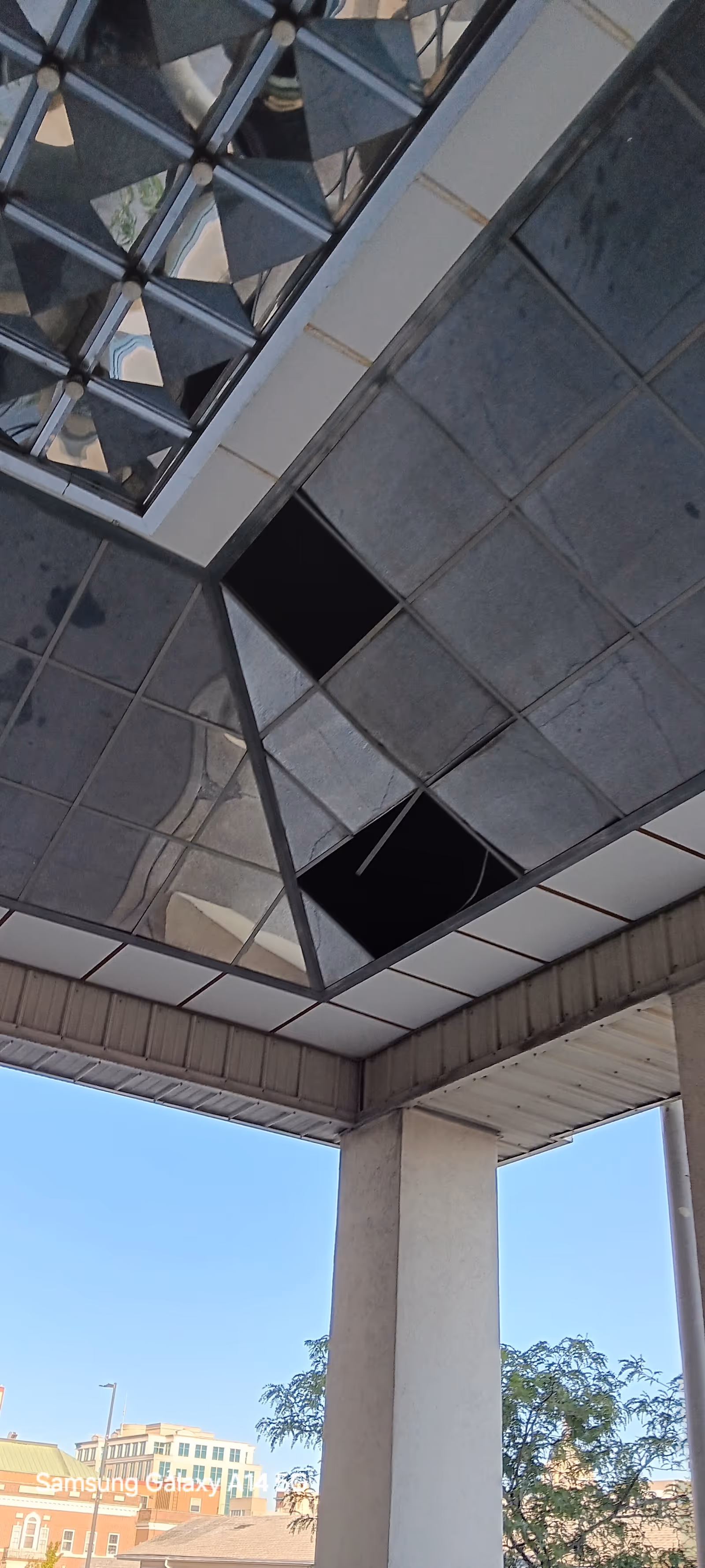 View of a modern building exterior with reflective panels, supporting columns, and blue sky.