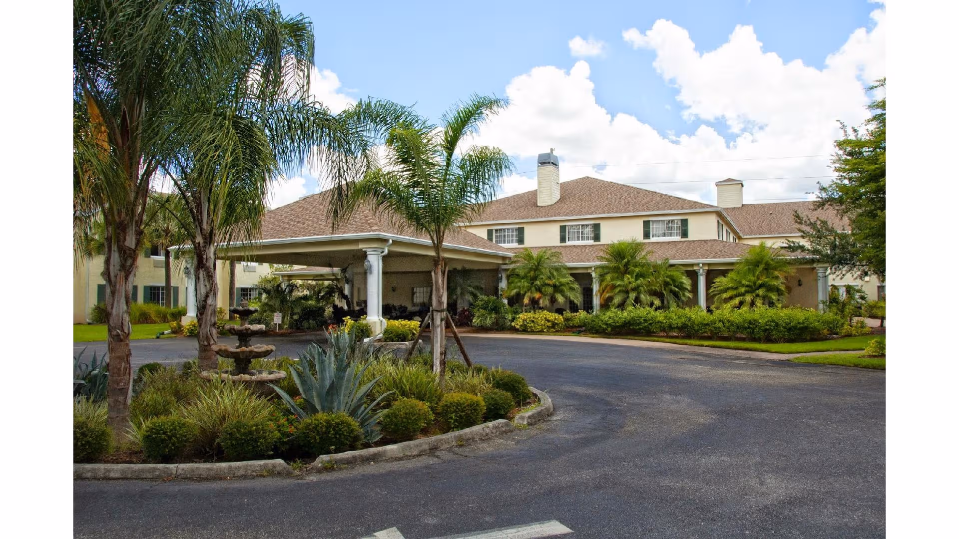 Two-story senior living facility with circular driveway, palm trees, and manicured landscaping.