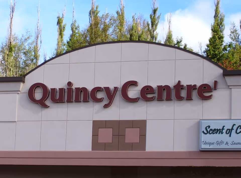 Exterior view of a building with a large QuincyCentre sign and trees behind.
