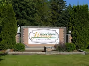 Brick entrance sign with greenery displays the facility name at the front.