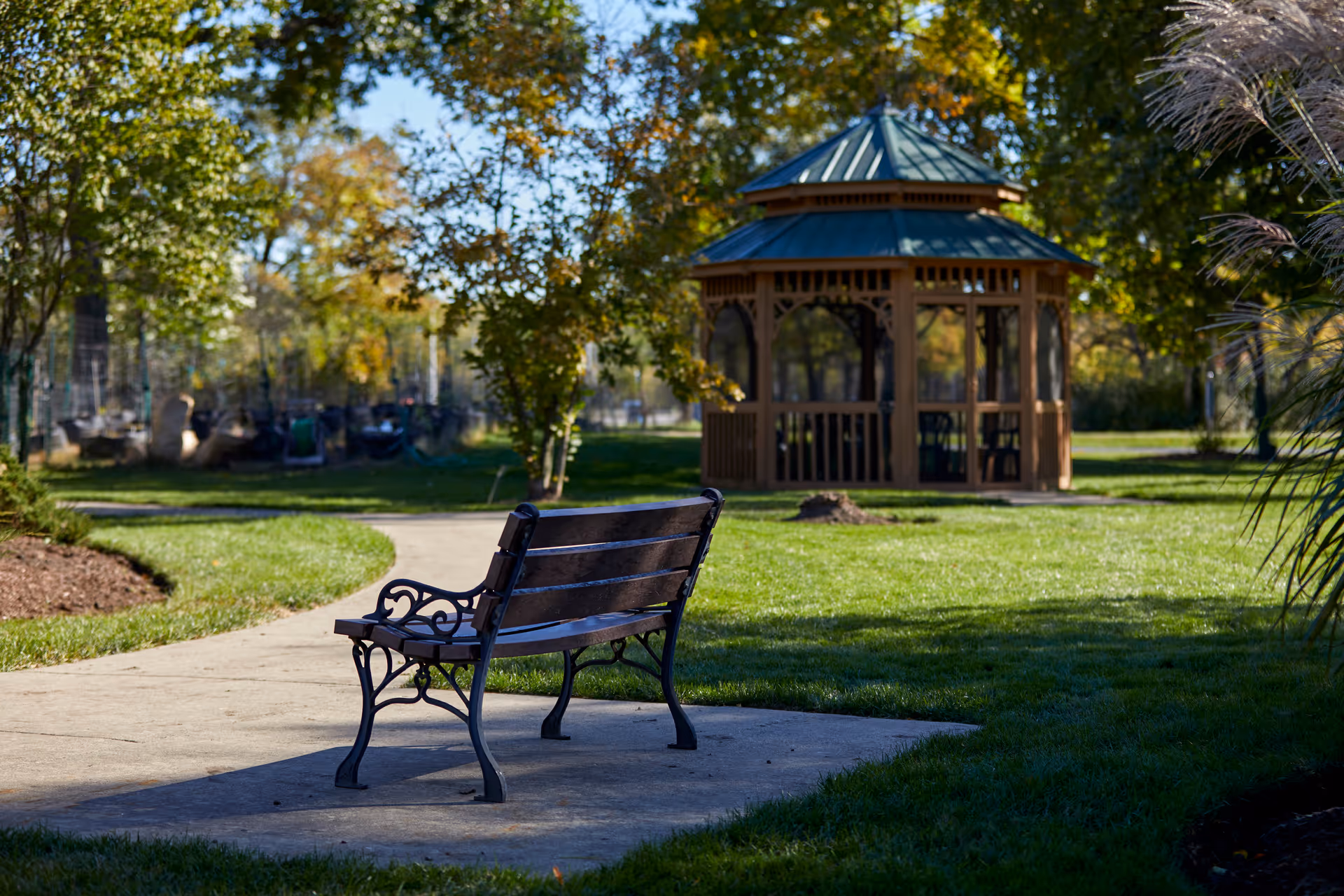 Park-like courtyard with an empty bench on a paved path and a wooden gazebo in the background.