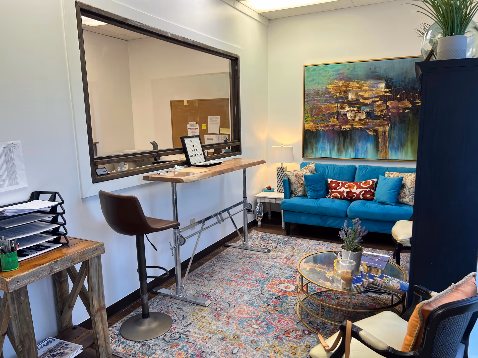 Bright senior living lounge with turquoise sofa, coffee table, and a workspace.