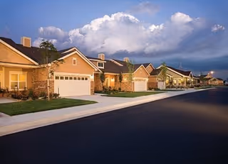 Row of beige, single-story buildings with garages along a sidewalk at dusk.