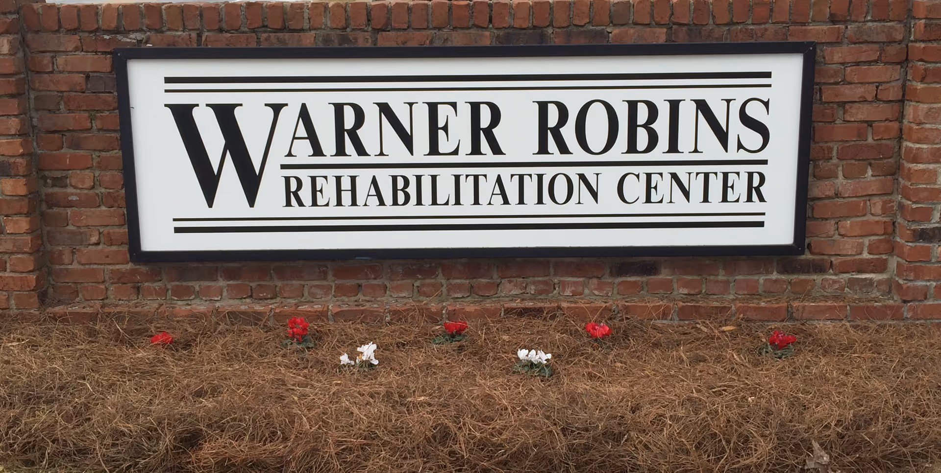 Exterior brick wall sign for Warner Robins Rehabilitation Center with a flower bed.