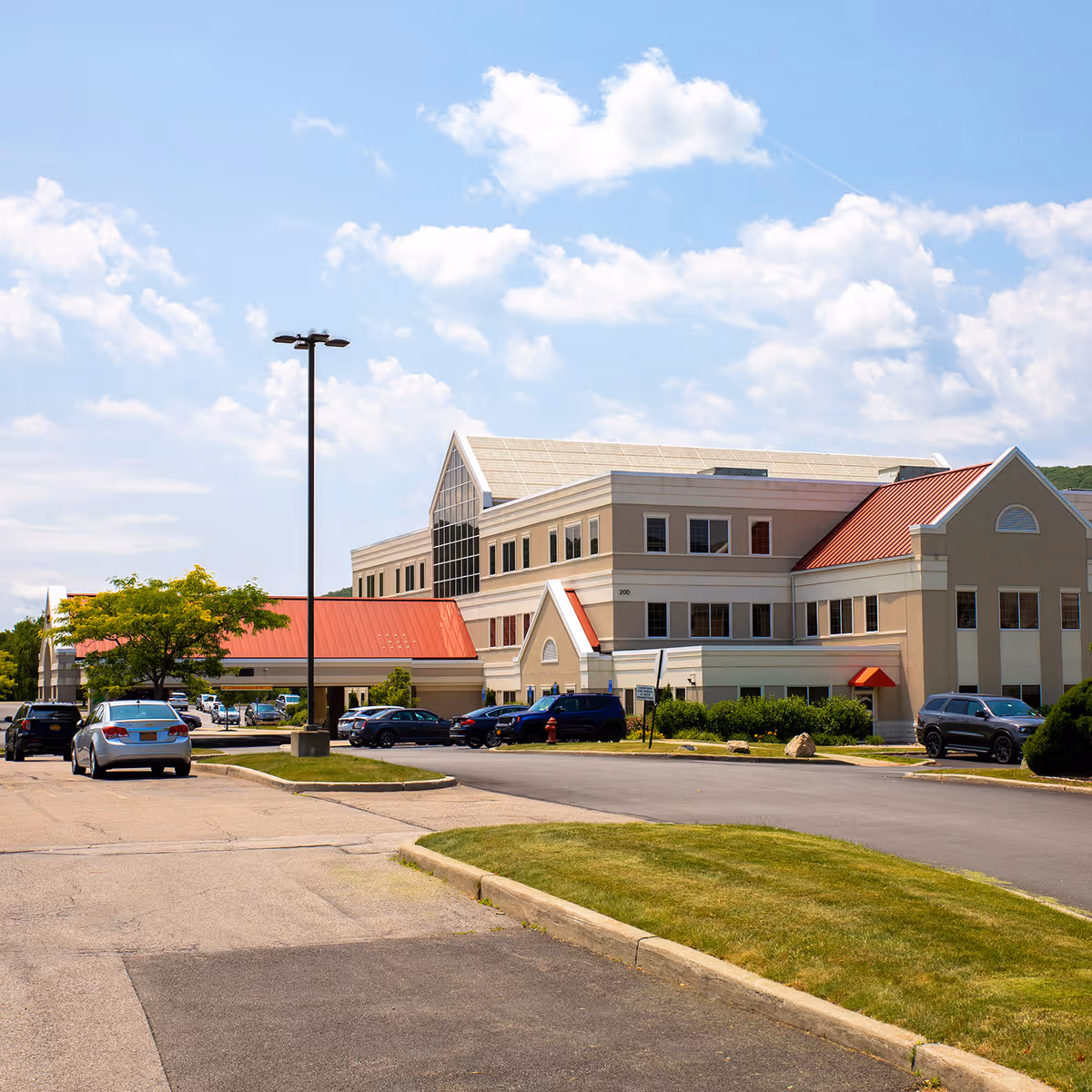 Exterior view of a large modern medical building with parking and greenery.